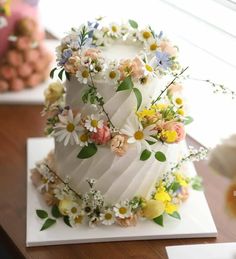 a three tiered cake decorated with flowers and greenery sits on a wooden table