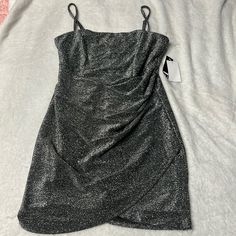 a shiny silver dress on a bed with a tag hanging off the back of it