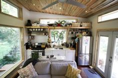 a living room filled with furniture next to a window and a refrigerator under a wooden ceiling