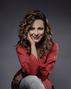 a woman sitting on top of a chair with her hand under her chin and looking at the camera