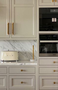 a kitchen with white cabinets and marble counter tops, gold pulls on the door knobs