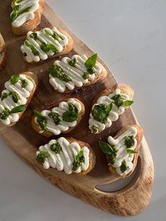 small appetizers are arranged on a wooden platter with green leaves and white icing