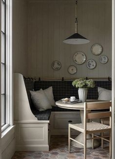 a table and chairs in a room with plates hanging on the wall above it, next to a window