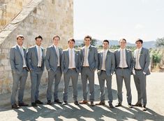 a group of men in suits standing next to each other on a dirt road near a stone wall