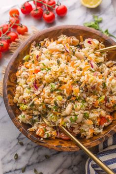 a wooden bowl filled with rice salad next to tomatoes and other vegetables on a marble surface