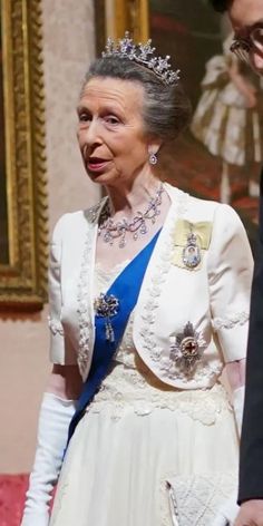 an older woman wearing a tiara standing next to a man in a suit and tie