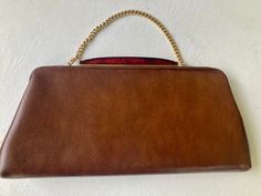 "60s  patent  leather clutch Red lucite handle  Gold tone hardware  Carry as a clutch or use the short chain, if used as a clutch the chain folds inside the bag Faux leather - vynp 12\"  wide at bottom  10\" wide at top 6\" high  1.5\" deep  10\"  chain  Condition - Very Good Vintage" Formal Brown Evening Bag With Chain Strap, Vintage Red Clutch For Formal Occasions, Brown Evening Bag With Chain Strap, Red Vintage Clutch For Formal Occasions, Brown Retro Clutch For Formal Occasions, Retro Brown Clutch For Evening, Vintage Brown Clutch For Party, Brown Clutch With Gold-tone Hardware, Leather Clutch With Gold-tone Hardware