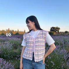 a woman standing in front of lavender flowers wearing a crocheted vest and smiling