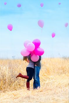 a man and woman walking through a field with pink balloons