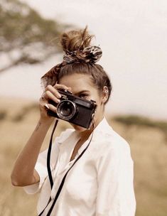 a woman holding a camera up to her face while standing in a field with tall grass