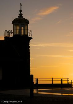 the sun is setting behind a light house