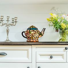 a glass teapot sitting on top of a counter next to candles and vases