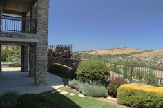 an outside view of a building with bushes and shrubs in the foreground, overlooking a valley