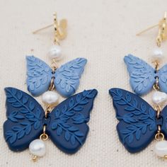 A Pleasant Thought Toronto, b. 2016 Shades of Blue, 2021Polymer clay and freshwater pearls on 14k gold-plated butterfly post studs Handcrafted, vintage-inspired clay earrings featuring two intricate butterflies in shades of blue dangling between lustrous freshwater pearls, and below a radiant butterfly stud. Adds flutter and whimsy to any look. PRODUCT DETAILS Each piece is unique and handcrafted in Canada – it’s wearable art! Polymer clay – long-lasting, unique, and ultra-lightweight on the ear Blue Clay Earrings, Clay Butterfly, Blue Polymer Clay, Blue Clay, How To Clean Metal, Clean Makeup, Butterfly Earrings, Blue Butterfly, Handmade Polymer Clay