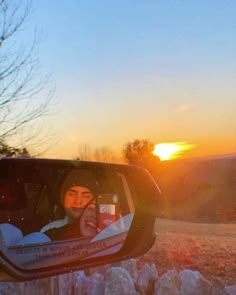 the reflection of a person in a car mirror at sunset with trees and snow on the ground