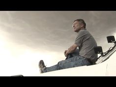 a man sitting on top of a white truck under a cloudy sky with his feet up