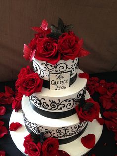 a three tiered wedding cake with red roses on the bottom and black trimmings