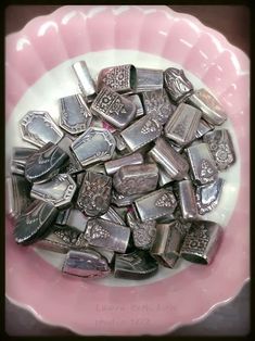 a pink and white bowl filled with lots of silver colored metal pieces on top of a table