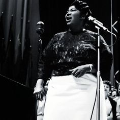 a woman standing in front of a microphone and singing into a microphone with an audience behind her