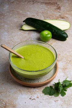 a glass bowl filled with green liquid next to cucumbers