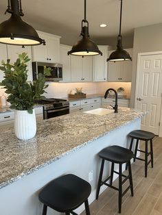 three stools are sitting at the bar in this kitchen with marble countertops and white cabinets