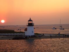 a light house sitting on top of a sandy beach next to the ocean at sunset