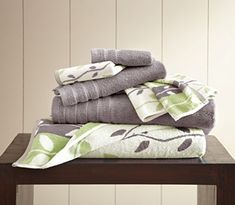 towels stacked on top of each other in front of a wooden table with white and green wallpaper