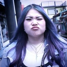 a woman with purple hair and piercings on her face is making a funny face