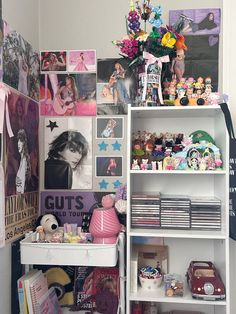 a white book shelf filled with lots of toys and pictures next to a wall covered in posters