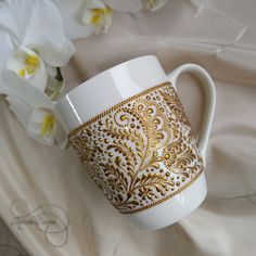 a white and gold coffee cup sitting on top of a table next to some flowers