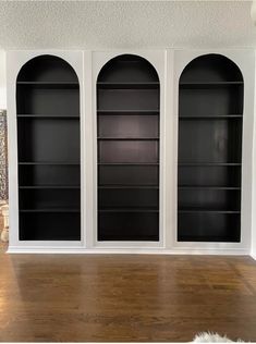 an empty room with three black bookshelves on the wall and wood flooring