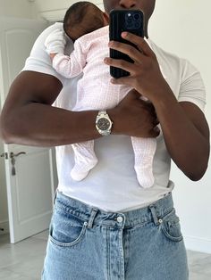 a man holding a baby in his arms and taking a selfie with a cell phone