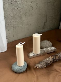 two candles sitting on top of a table next to some rocks and a tree branch