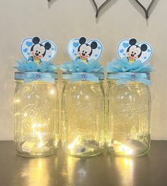 three mason jars with lights in them and mickey mouse tags on the lids, sitting on a table