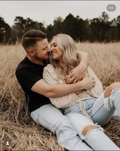 a man and woman are sitting in the middle of some tall grass, one is kissing the other's forehead