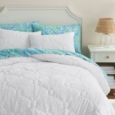 a white bed with blue and green comforter in a bedroom next to a night stand