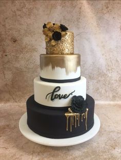 a three tiered cake with gold and black decorations on the top, decorated with flowers