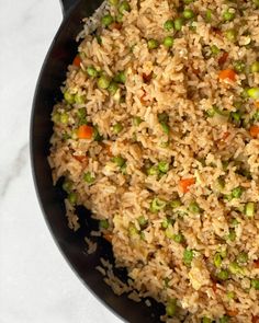 rice with peas and carrots in a skillet on a marble counter top, ready to be eaten