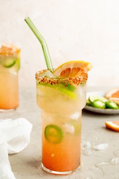 two glasses filled with drinks and garnished with lime, oranges and cucumbers