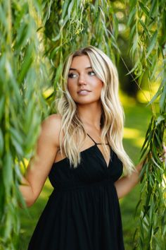 a beautiful blond woman standing in front of some green leaves and looking at the camera