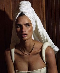 a woman with a towel on her head wearing a white dress and gold chain necklace