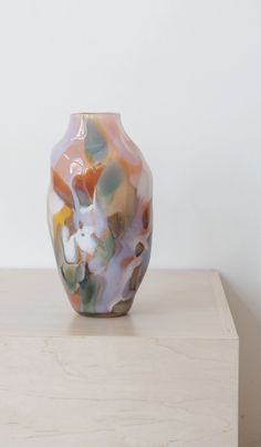 a colorful vase sitting on top of a wooden table next to a white wall in a room