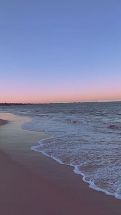 an ocean beach with waves coming in to the shore and a pink sky above it