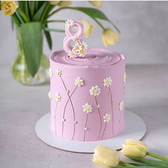 a pink cake decorated with flowers and the number eight on top is next to tulips