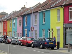 a row of multi - colored houses with cars parked on the side of the street