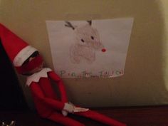 an elf is sitting next to a piece of paper with a drawing of a deer on it