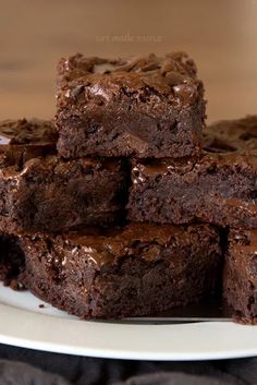 chocolate brownies stacked on top of each other on a white plate with a black cloth