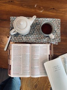 an open book and cup of tea on a wooden table