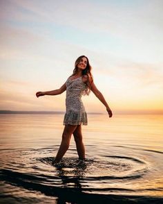 a woman standing in the water at sunset