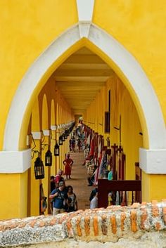 several people are walking through an archway with many umbrellas on the sides and yellow walls